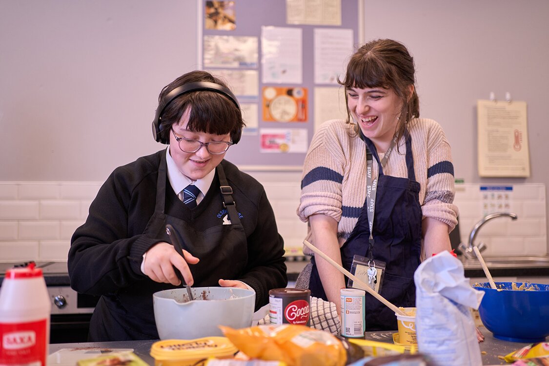 girl in school uniform using spoon to stir mixing bowl 