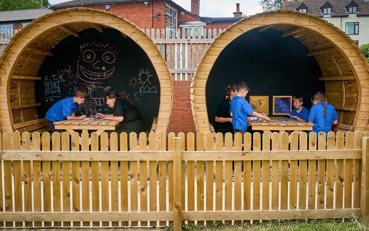 groups of children sat in outdoor wooden pods 