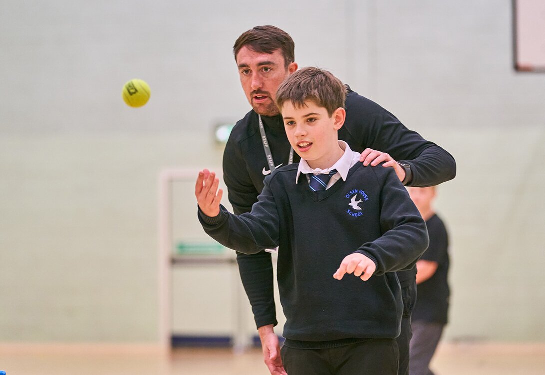 school pupil throwing a ball with an adult behind