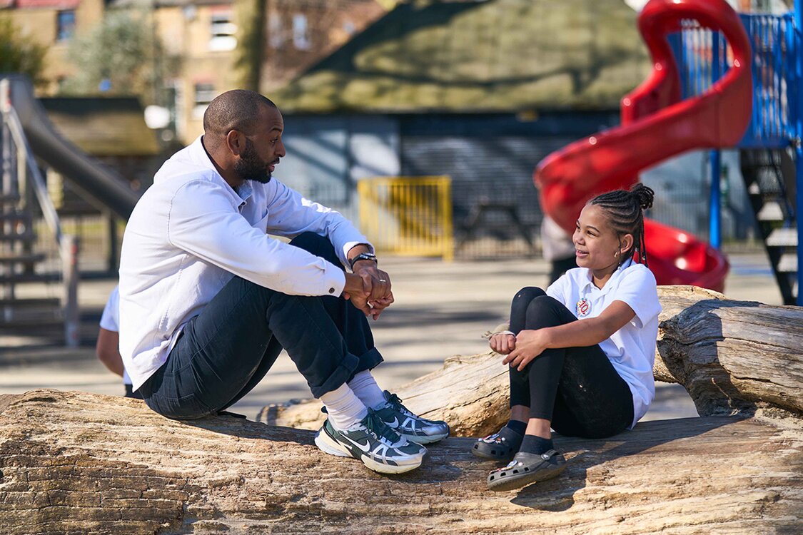adult and child sat talking on fallen tree trunk in park