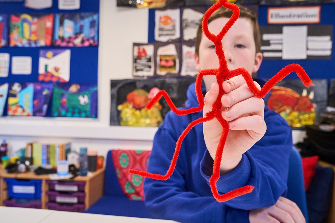 child holding a stick man up made from pipe cleaners