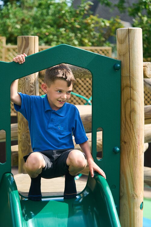 child in school uniform about to go down a slide