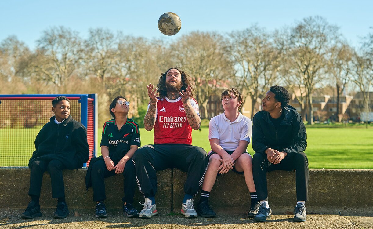 pupils and adult sat on a wall looking up as ball us thrown into the air