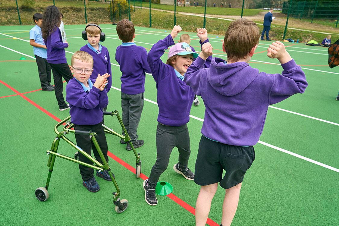 a group of children in school uniform on a sports court one child using a walking frame