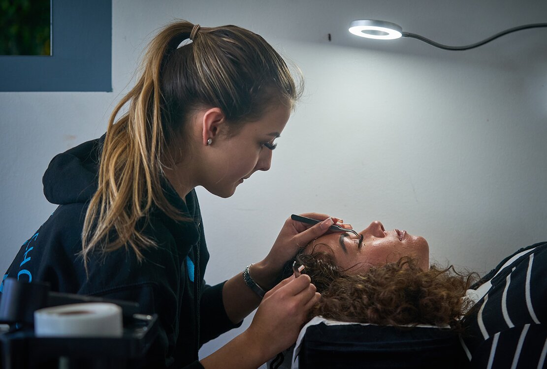 a pupil attends to an adults eyelashes under a lamp
