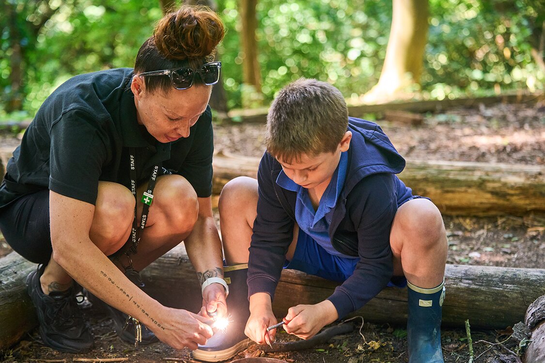 pupil and adult work together to light a fire