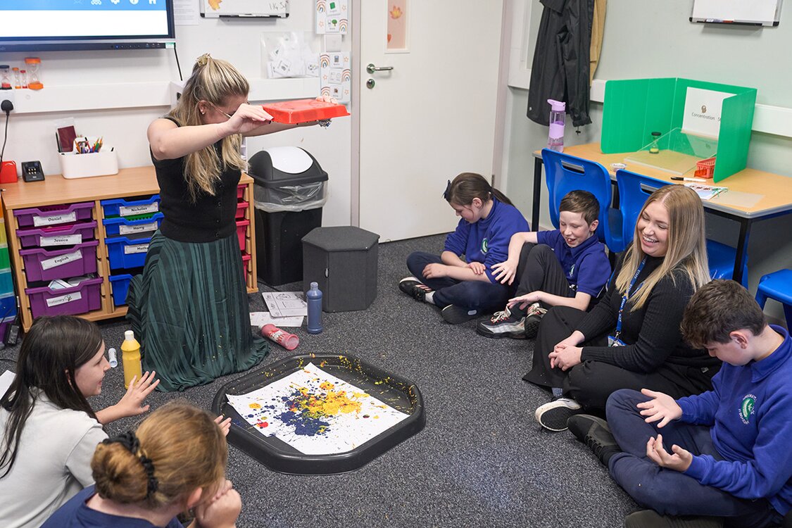 children sat on floor watching adult slattering paint into a tray