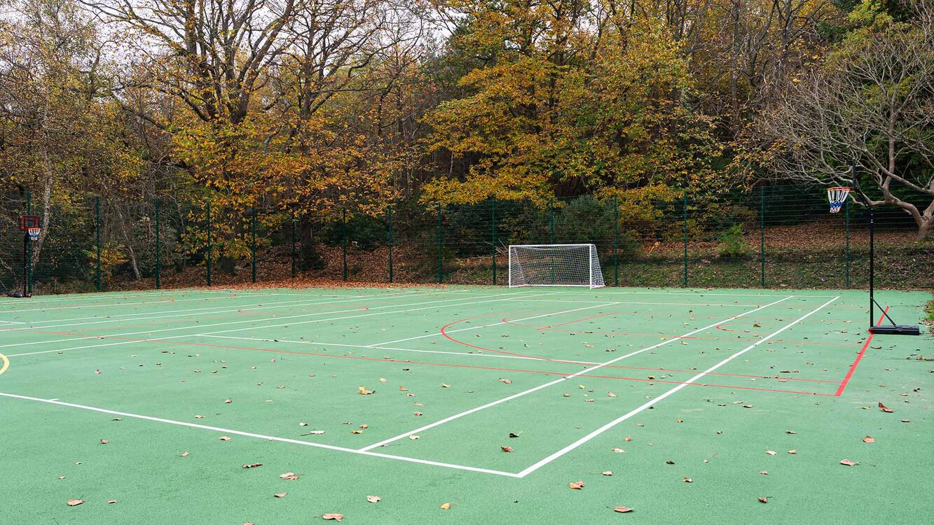 Out door multi use sports court in green with white lines and trees surrounding it