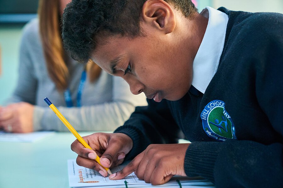 pupil sat a table writing on paper and using his finger as a space