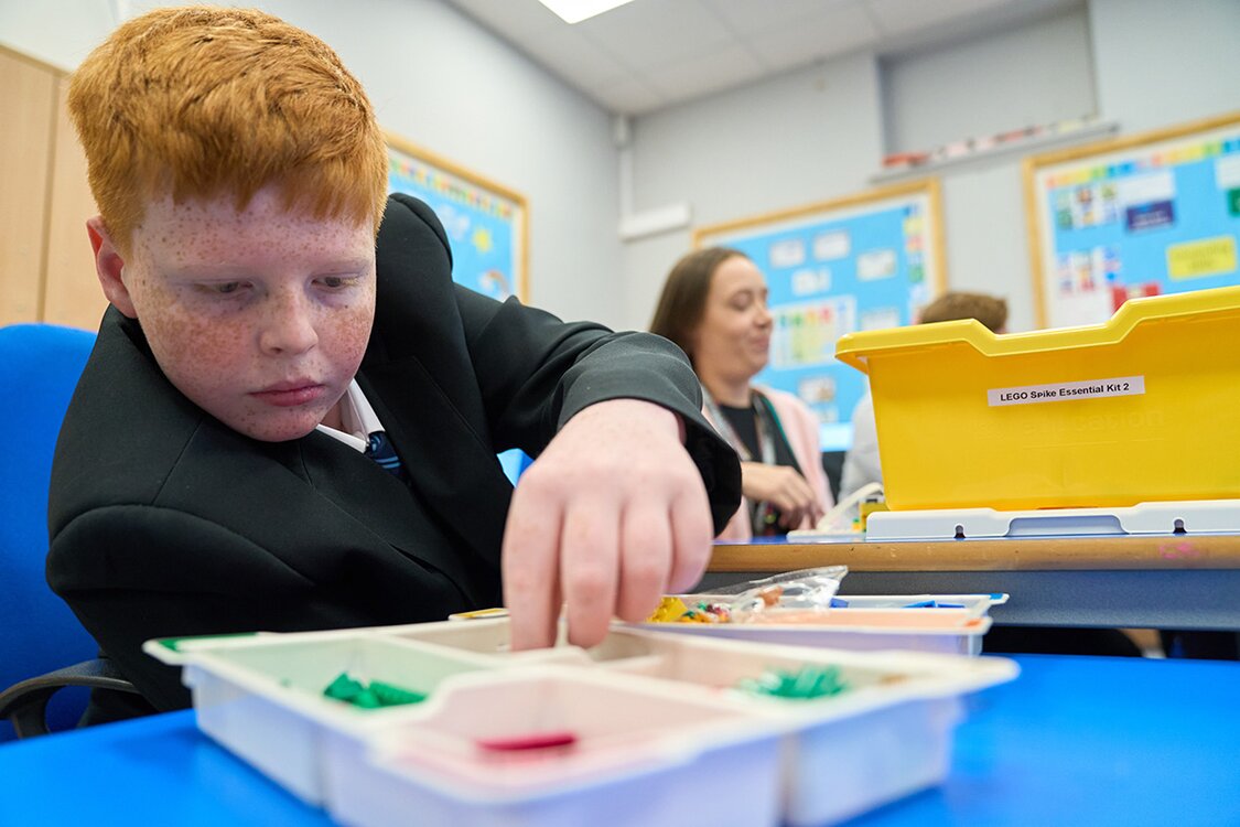 child in school uniform picks lego pieces from a container