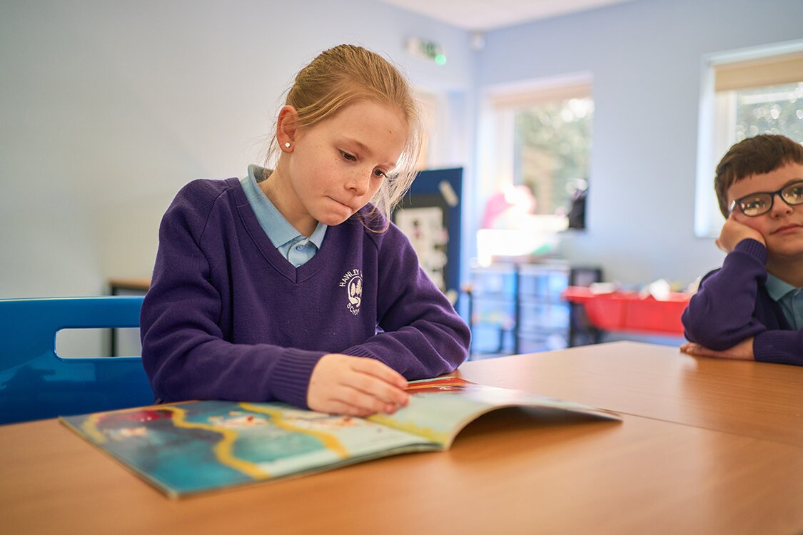 child in school uniform sat at a desk reading