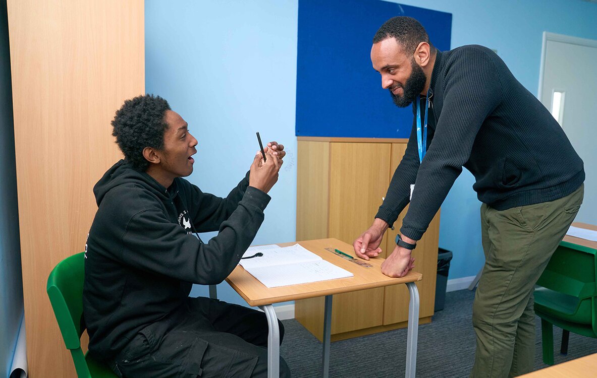 child at a desk looks up to an dult to talk