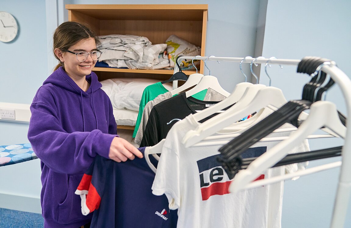 child in school uniform hangs clothing up on coat hangers