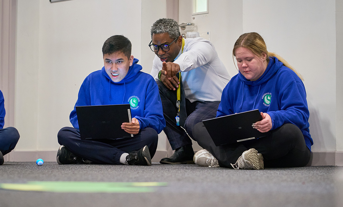 pupils with laptops take instruction from a teacher