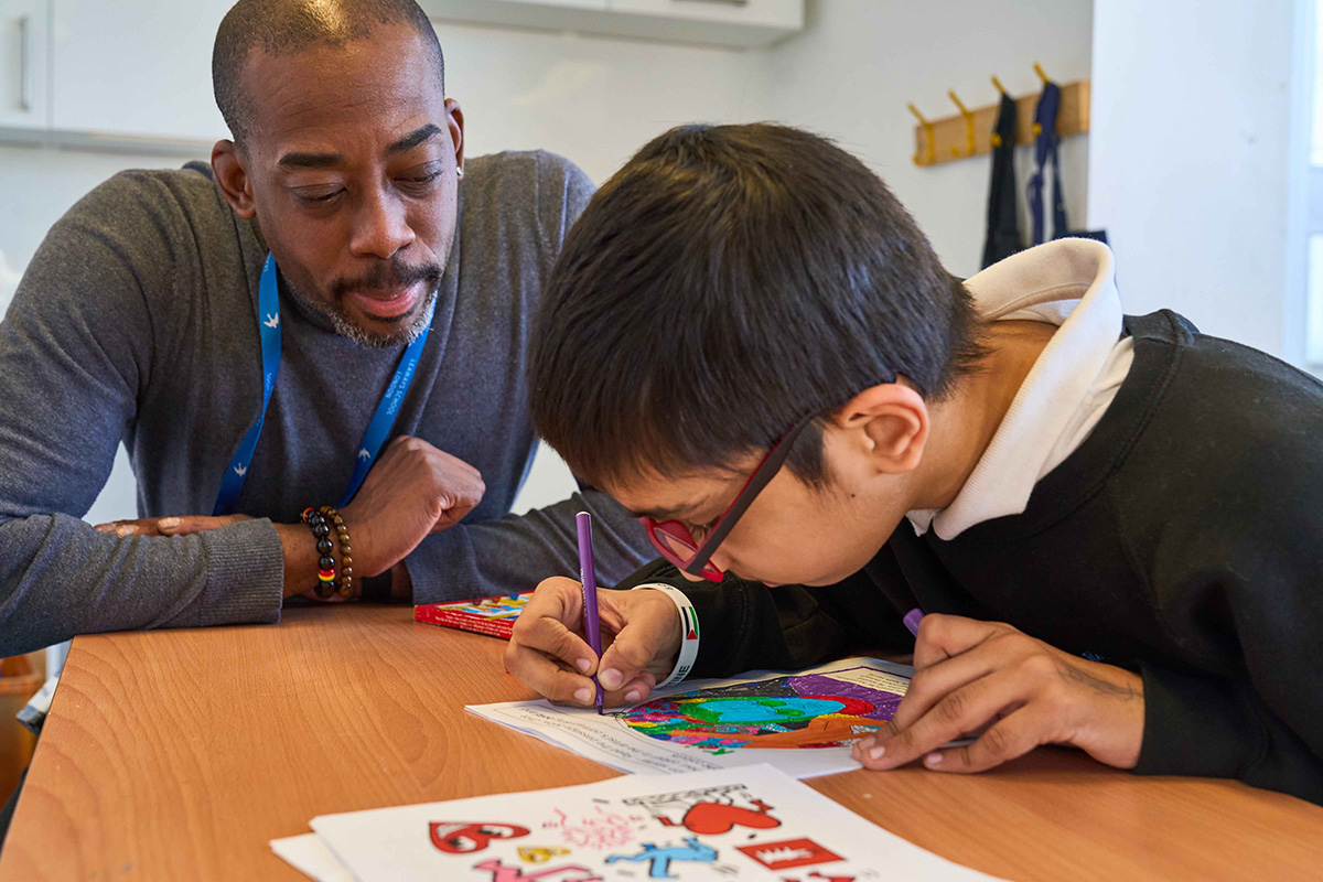 boy colouring in watched by adult