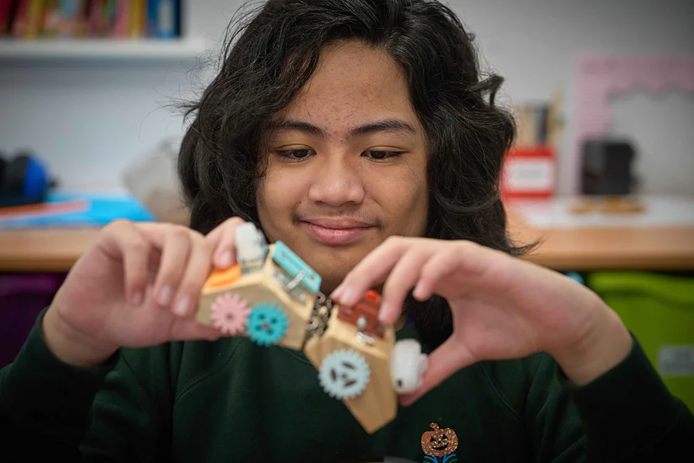 Pupil using a wooden fiddle toy with cogs and buttons