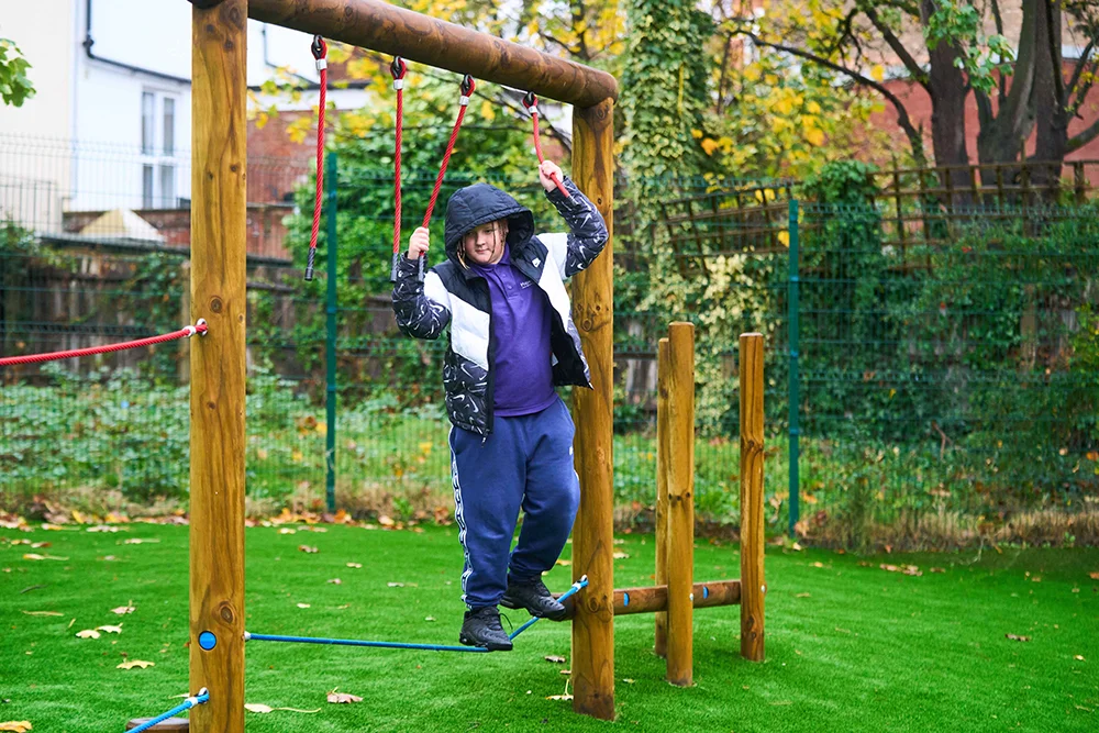 Pupil climbing across a rope bridge on outdoor play equipment
