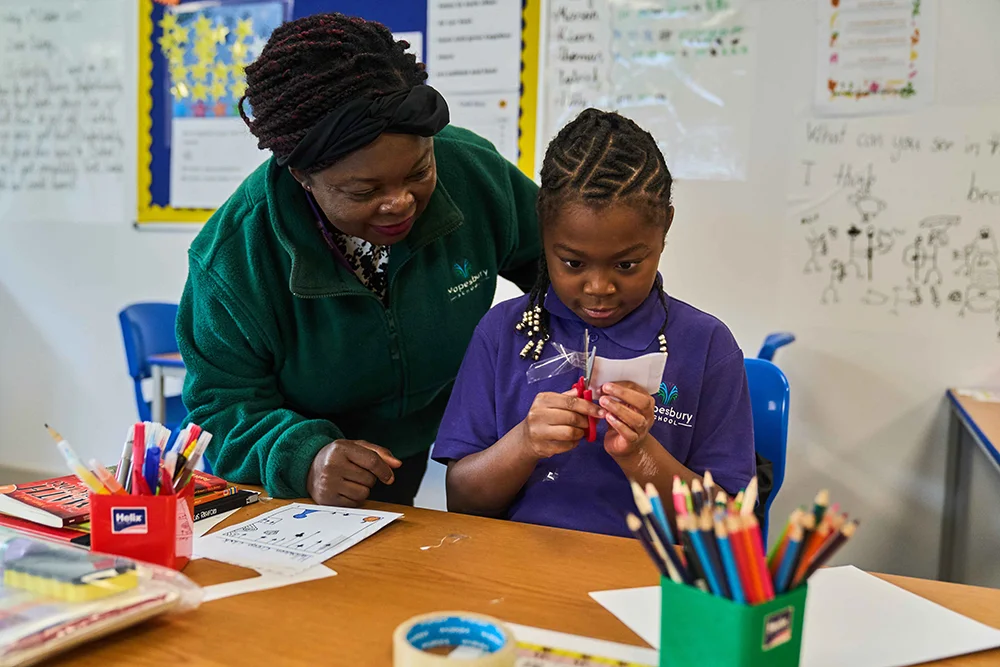Pupil using scissors supported by staff member