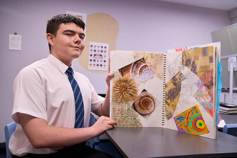 Pupil showing his art workbook with a collage of colourful work