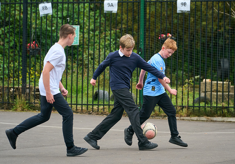 Three pupils playing football on the playground