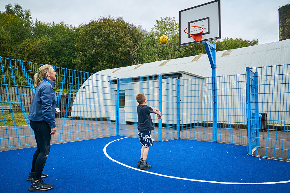 A pupil and teacher play basketball on a blue sports court