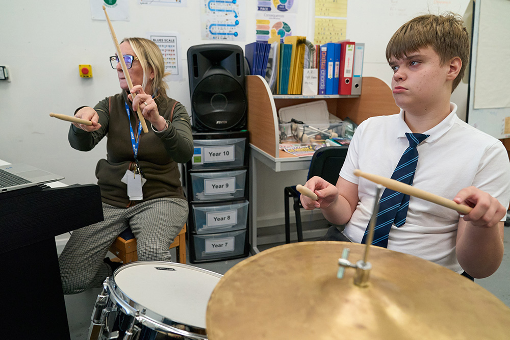 Teacher and pupil playing the drums with drum sticks