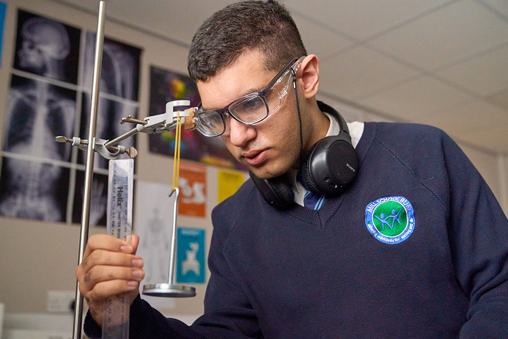 Pupil with safety goggles examining scientific apparatus 