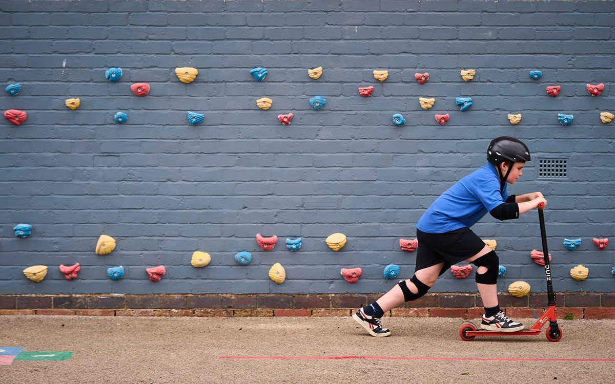 child on scooter races across in front of a climbing wall
