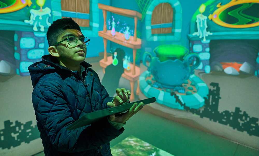 pupils holding computer keyboard in room with projected images on walls