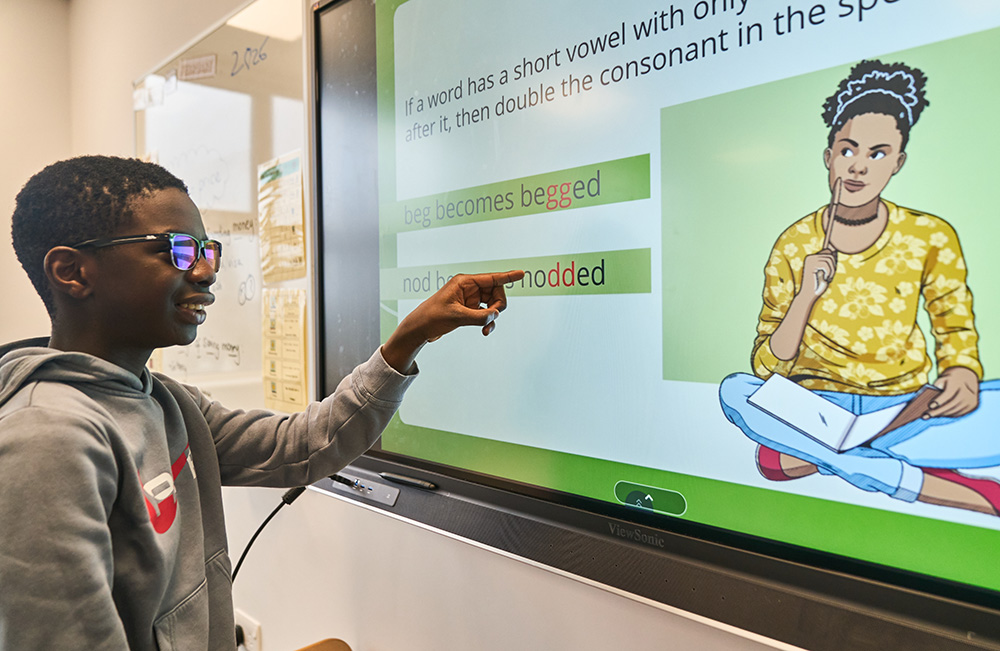 pupil wearing glasses points at tv on wall