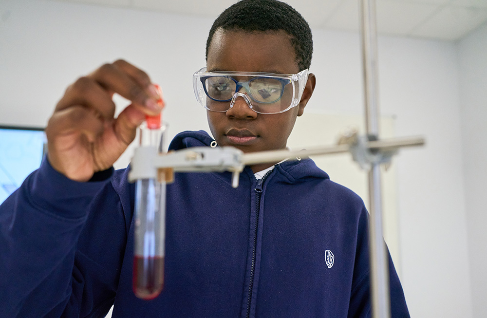 pupil wearing safety goggles adds liquid to test tube