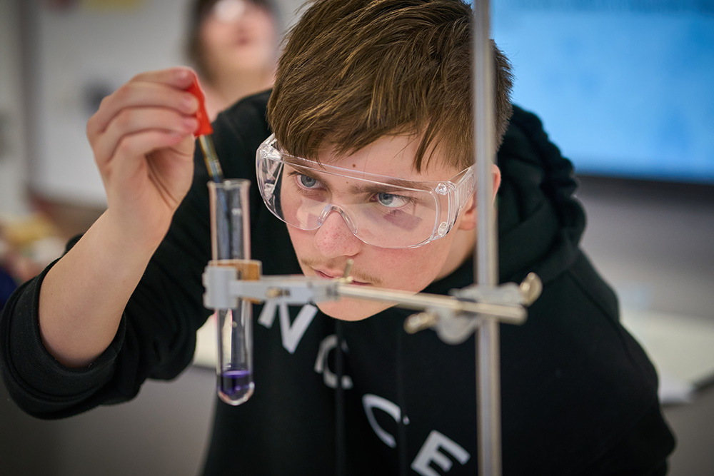 pupil wearing safety googles adds liquid to test tube with a dropper 