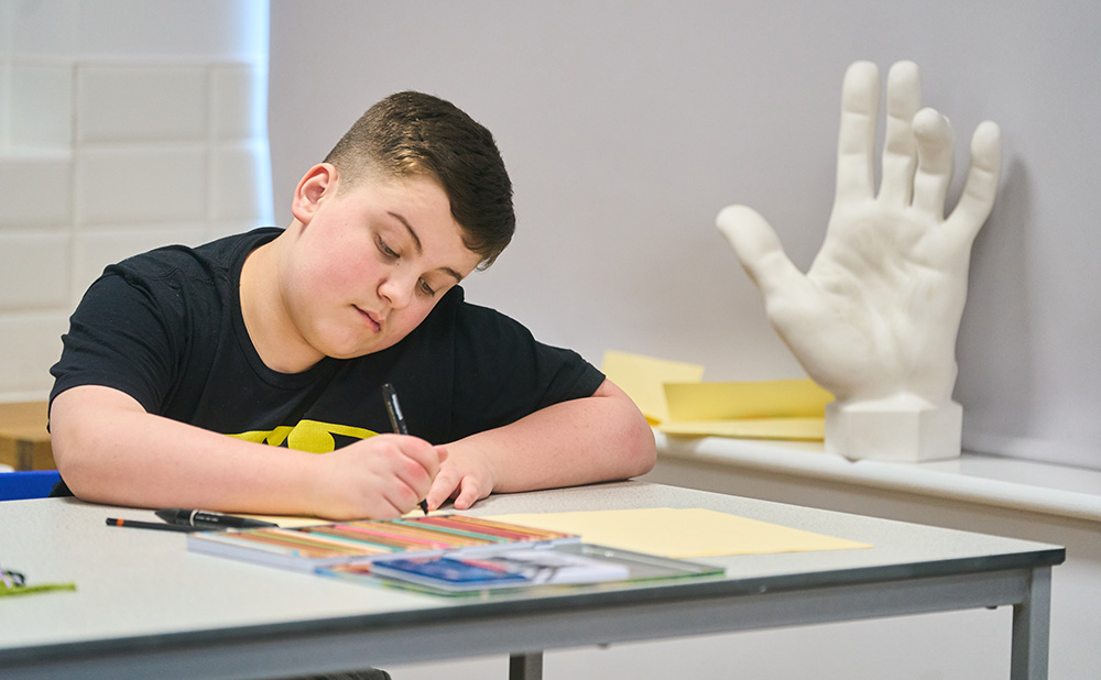 pupil works a desk with statue of hand behind