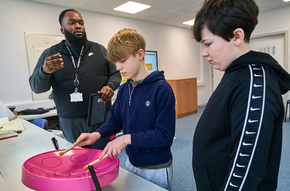 two pupils play pink steel pans with an adult